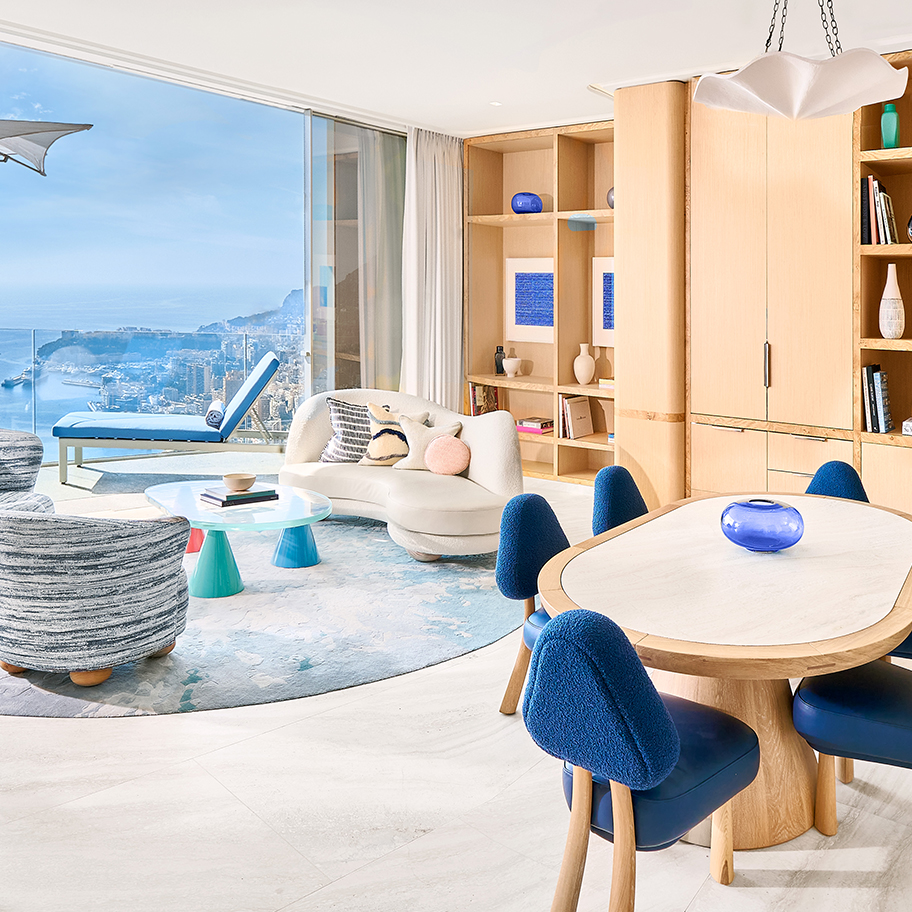 Salon avec un canapé blanc, une table basse en verre, une table de salle à manger avec des chaises bleues et une terrasse avec un transat et la vue sur la Côte d'Azur