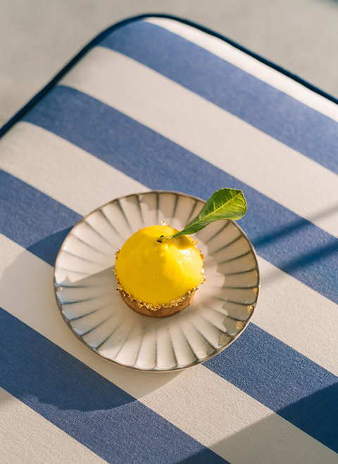 Une tarte au citron en trompe l'oeil servie dans une assiette posée sur une nappe rayée bleu et blanc.