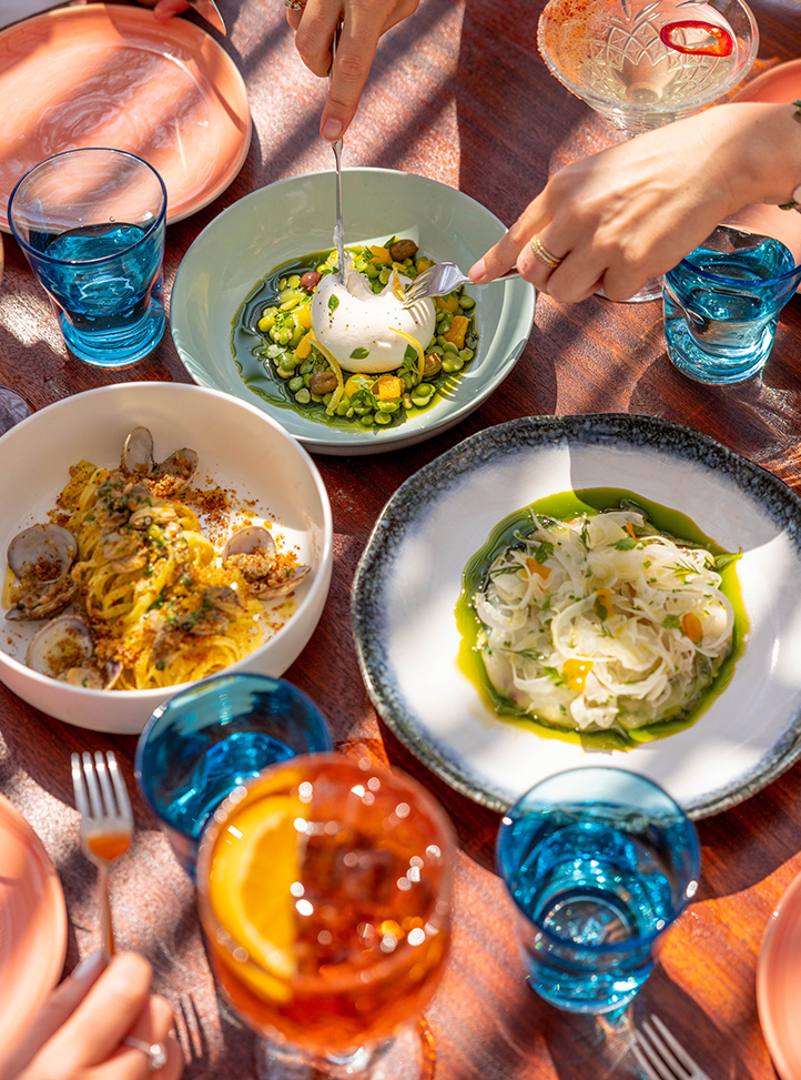 Trois différents plats sur une table de Maybourne La Plage avec des verres bleus.